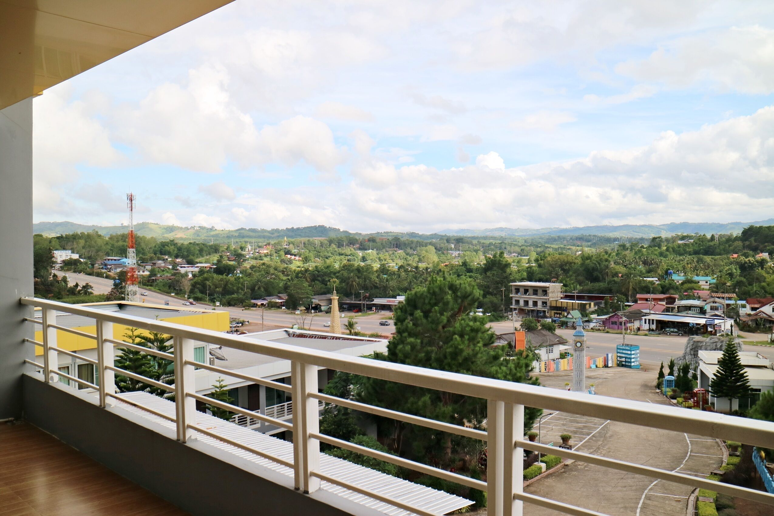 A balcony with a view of a town, including buildings, a road, and distant hills.