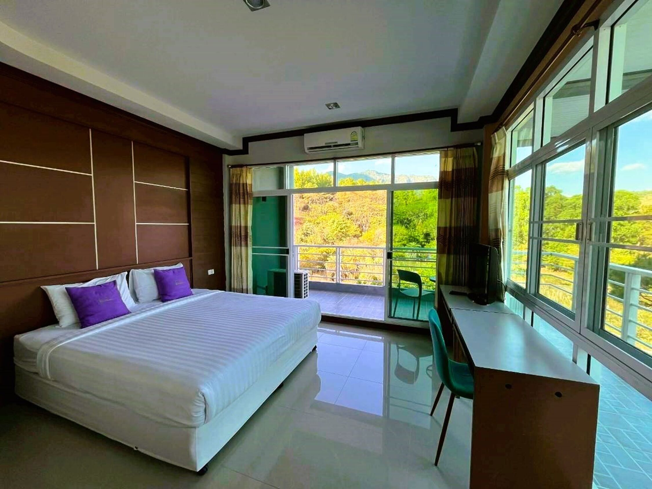 Habitación de hotel moderna con una cama grande, un escritorio y vistas a un paisaje verde a través de las ventanas.