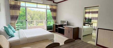 A hotel room with a bed, a desk, a TV, and a balcony with a view of the forest.
