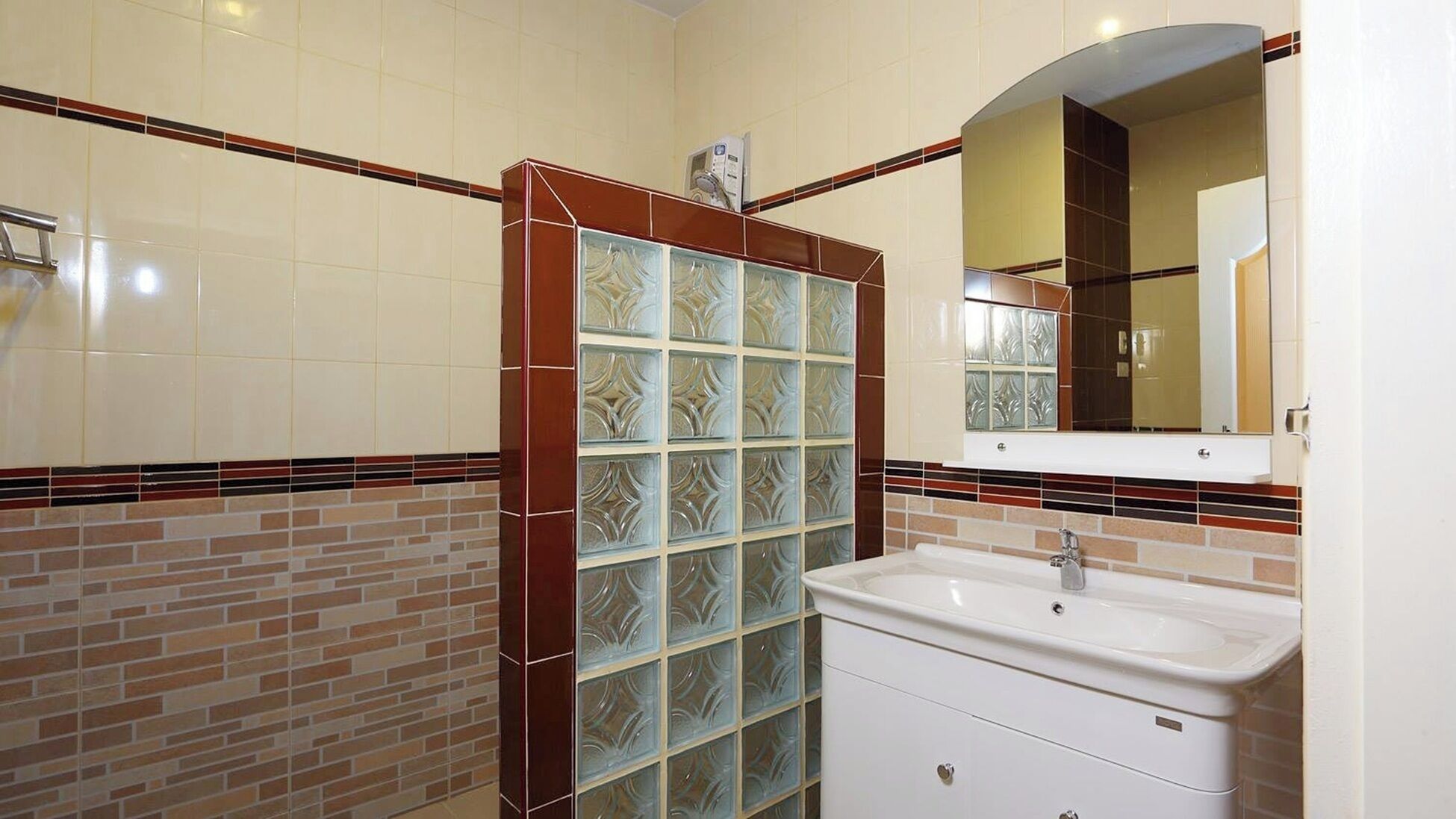 A bathroom with a tiled wall, a glass shower enclosure, a sink, and a mirror.