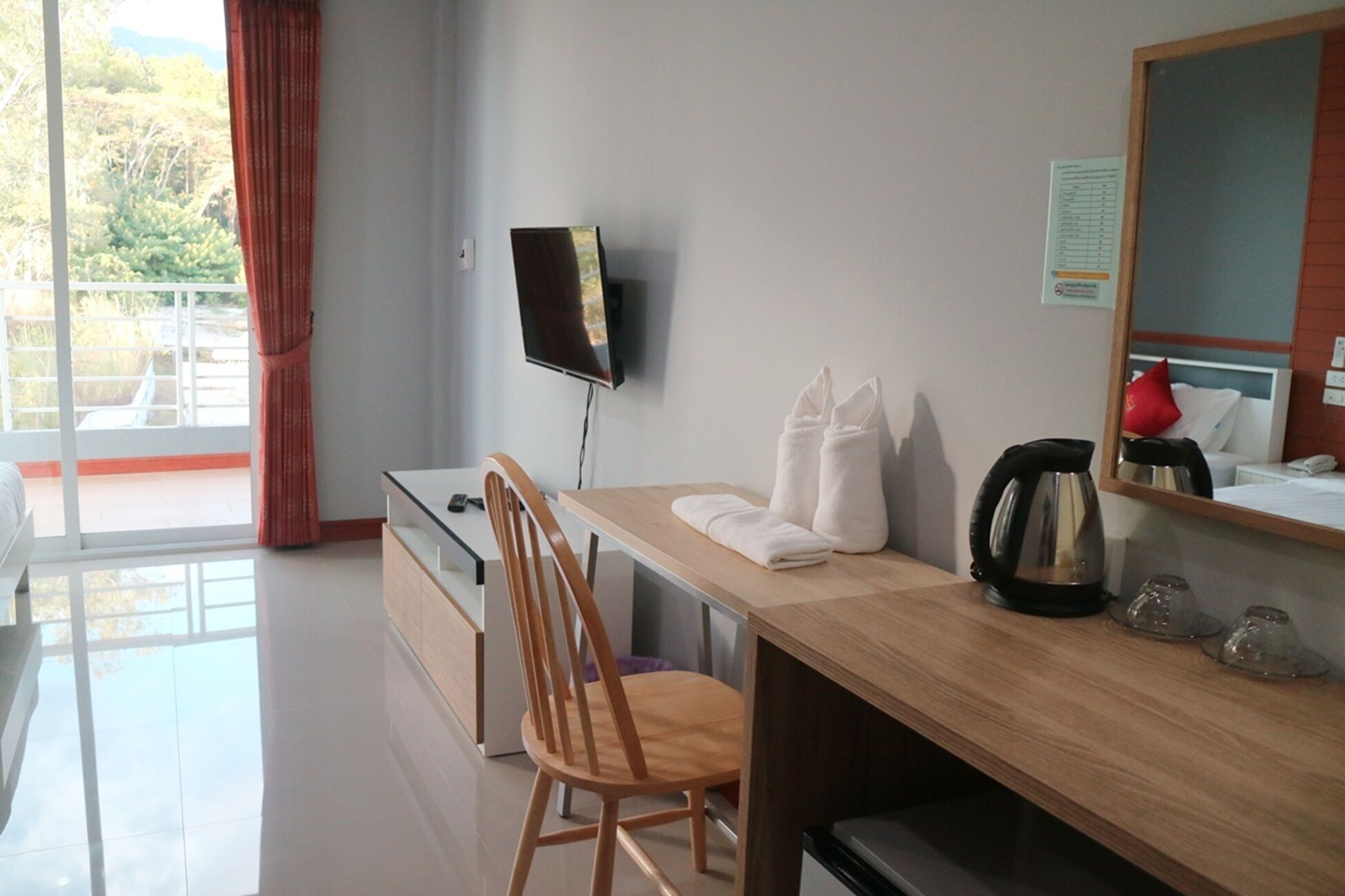 Une chambre d’hôtel avec un bureau en bois, une chaise, un téléviseur fixé au mur et une fenêtre avec des rideaux.