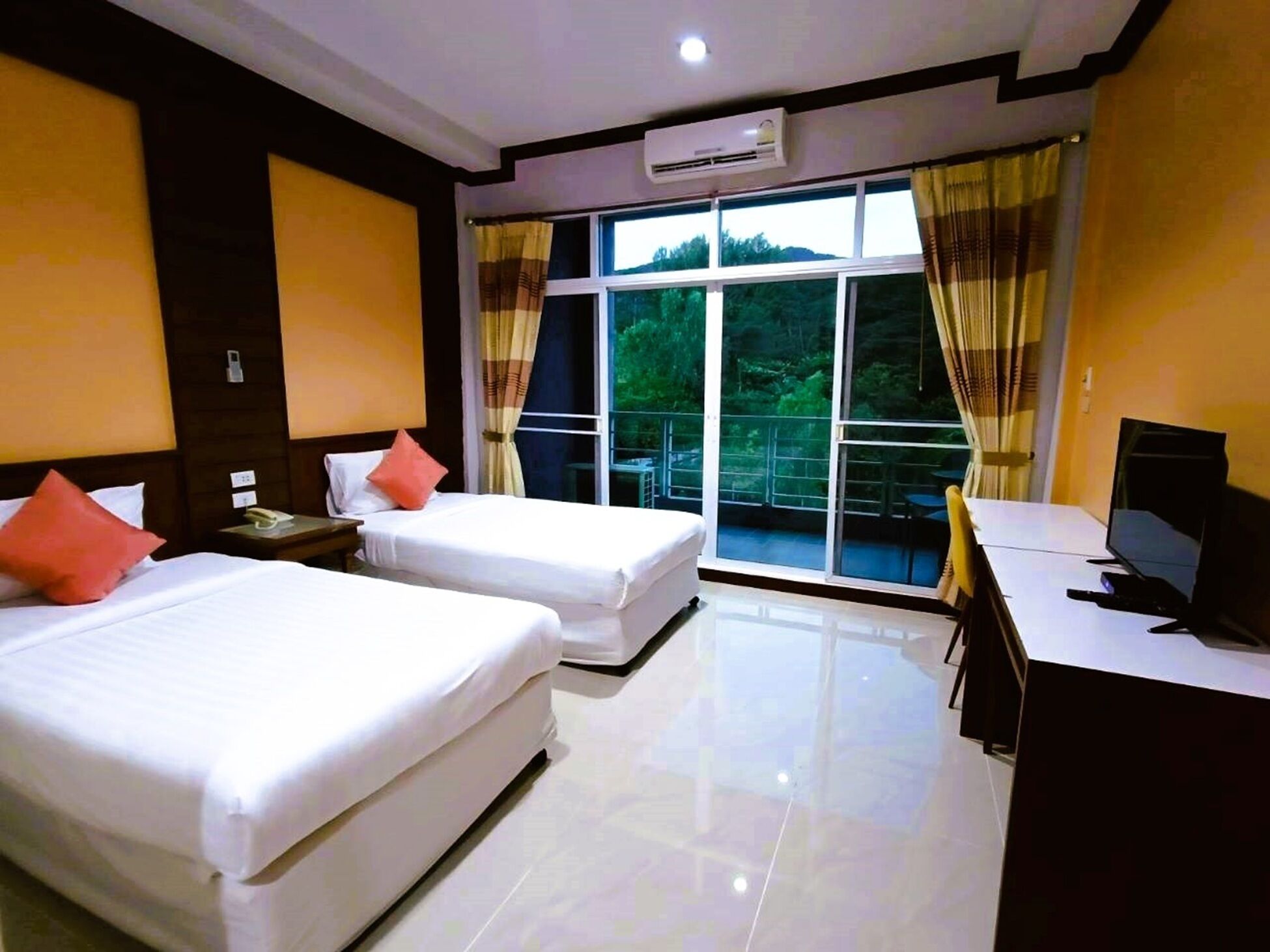 A hotel room with two beds, a desk with a computer, and large windows with curtains.