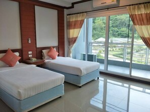 Een hotelkamer met twee bedden, een groot raam met gordijnen en uitzicht op groen.