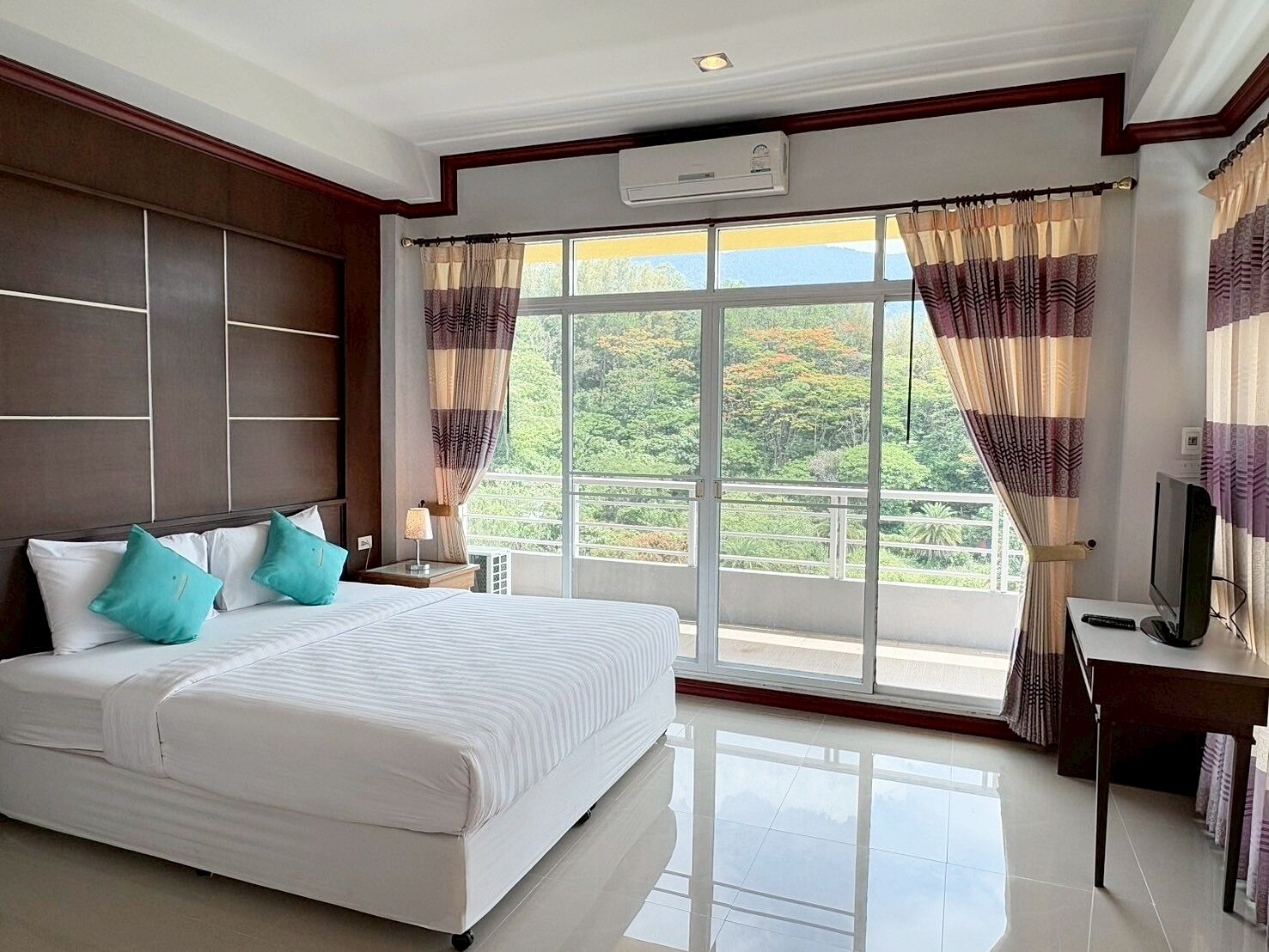 Una habitación de hotel con una cama grande, un televisor y un balcón con cortinas.