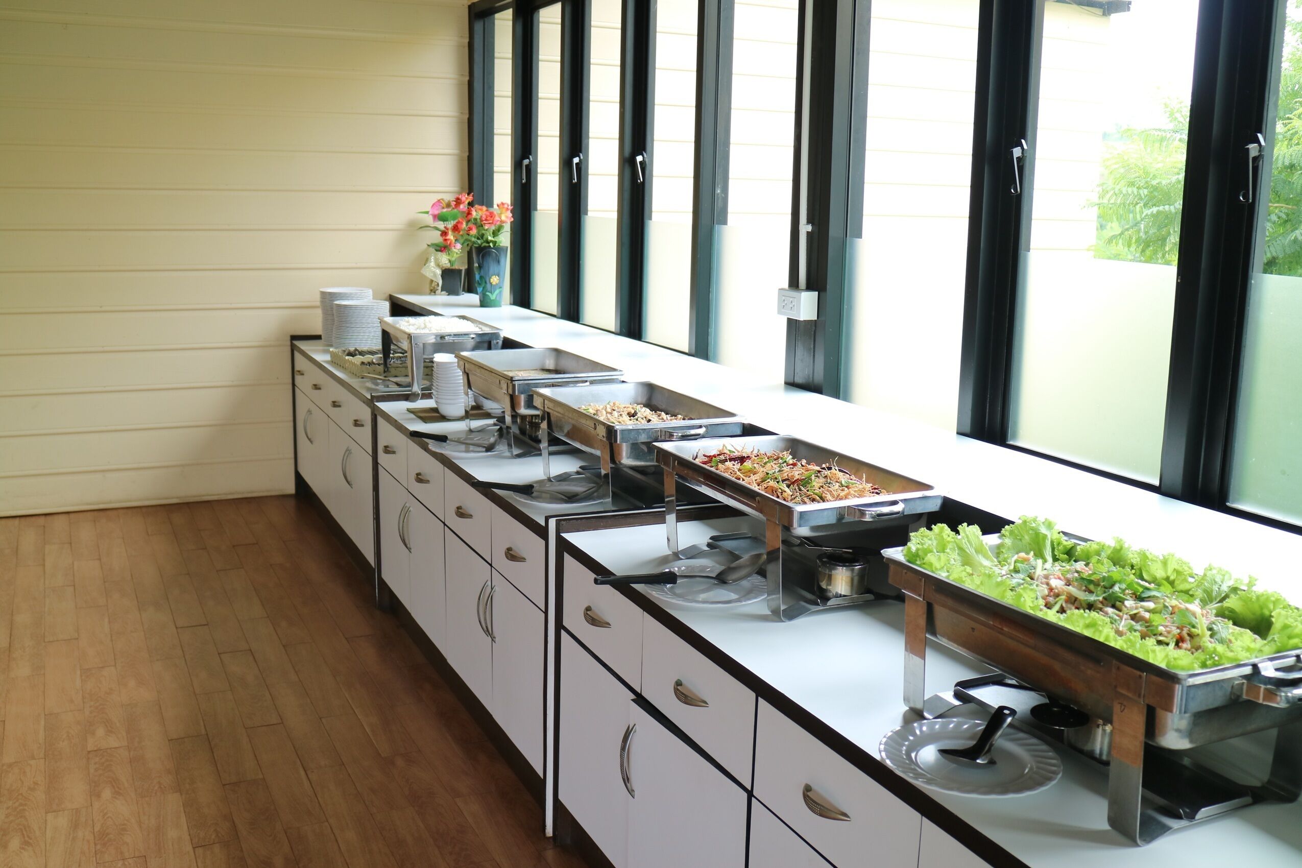 A buffet setup with multiple serving stations, a wooden floor, and a window with blinds.