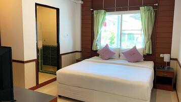 Una habitación de hotel con cama, mesita de noche, lámpara y ventana con cortinas.