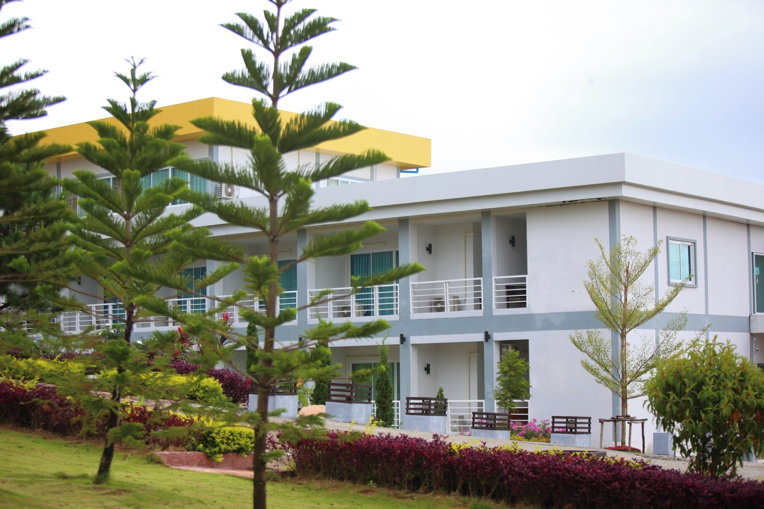 Um edifício moderno com telhado plano, várias varandas e um jardim bem cuidado com diversas plantas.