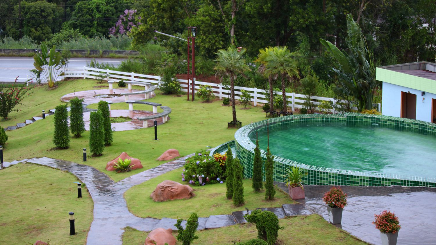 Una piscina rodeada por una cerca blanca, con un sendero que lleva a un edificio.