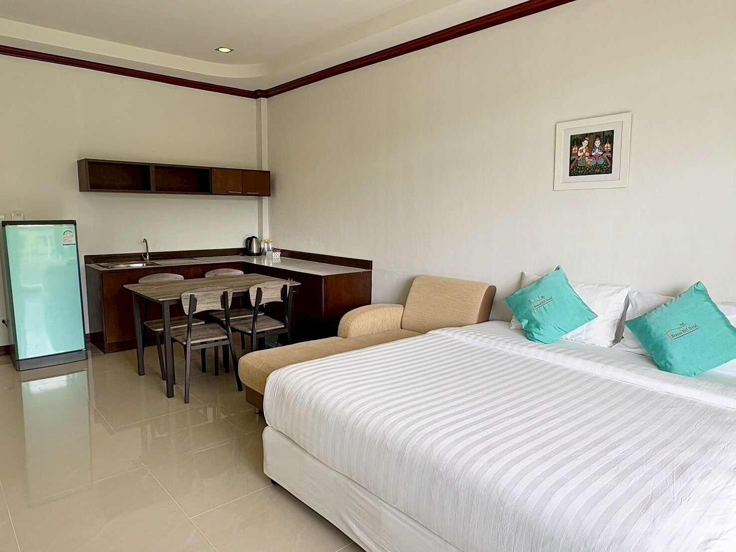 Habitación de hotel con cama, una pequeña kitchenette, una mesa de comedor con sillas y un refrigerador.