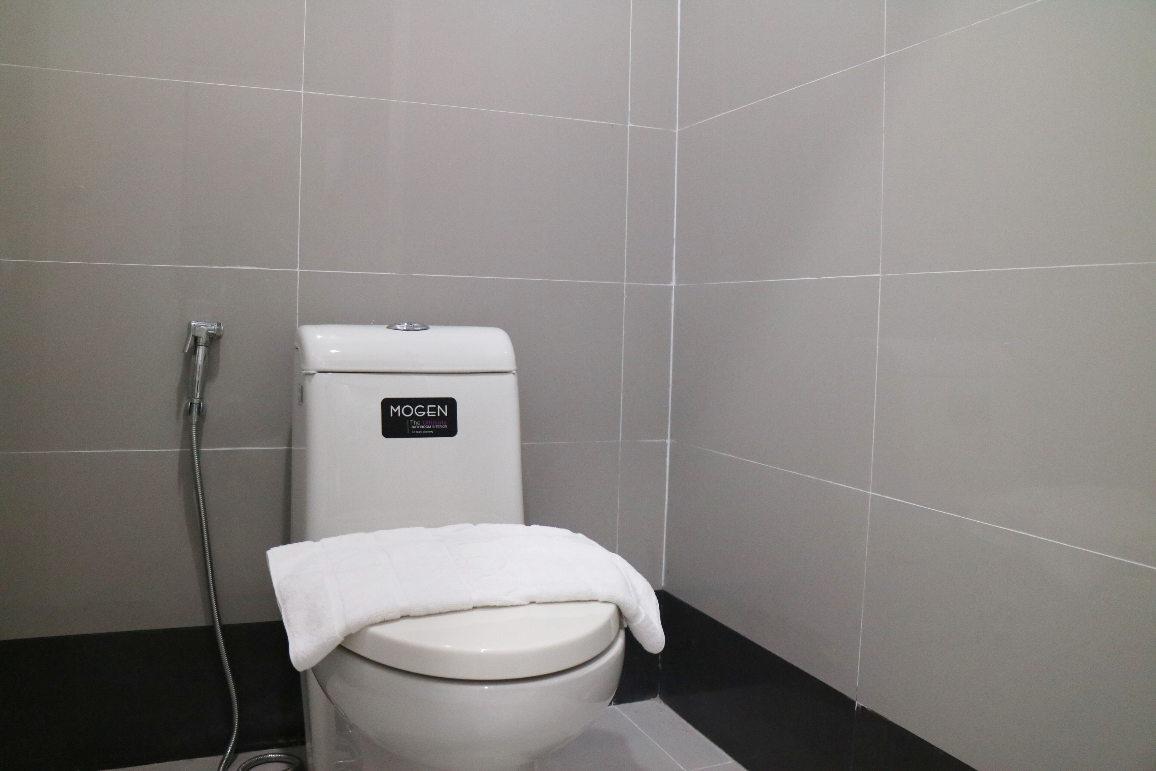 Et badeværelse med et hvidt toilet, en bruser og en sort gulv.