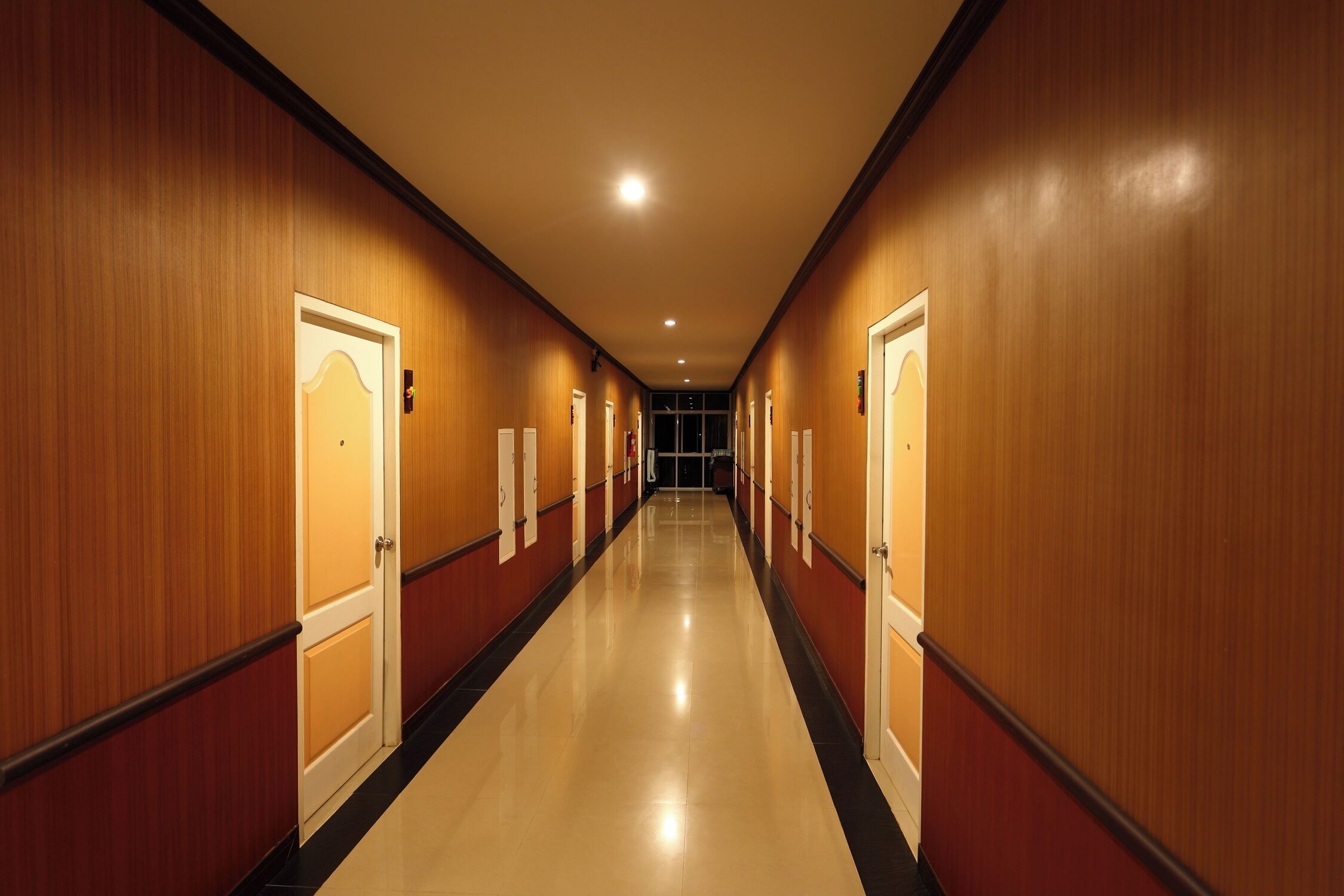 A hotel corridor with wooden walls and doors, a shiny floor, and recessed lighting.