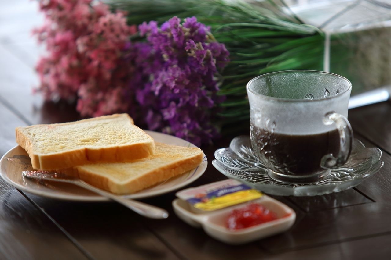 A plate with two slices of toast, a glass of dark liquid, and a small dish with red jam on a wooden table.