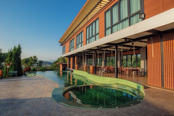 A modern building with a pool, outdoor seating, and a view of the landscape. - Breezehill Khao Kho Hotel (Khao Kho)