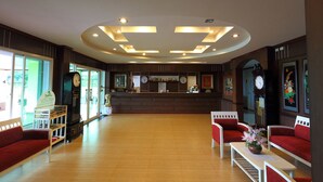 Een hotel lobby met een receptiebalie, houten vloeren, rode bekleden zitplaatsen en een grote wandklok.