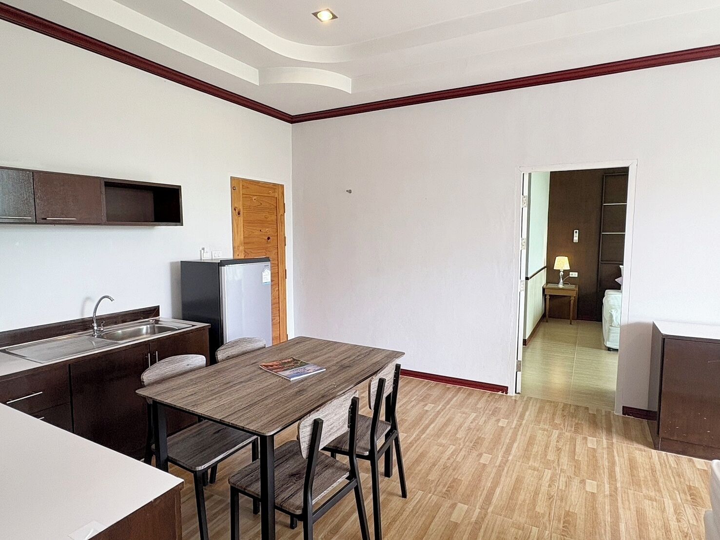 Cocina compacta con comedor, piso de madera y puerta visible que da a un dormitorio.