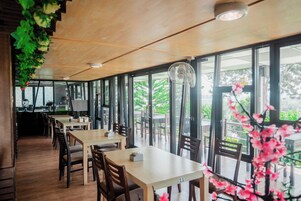 Un restaurante con mesas y sillas de madera, ventanas amplias y un ventilador de techo.