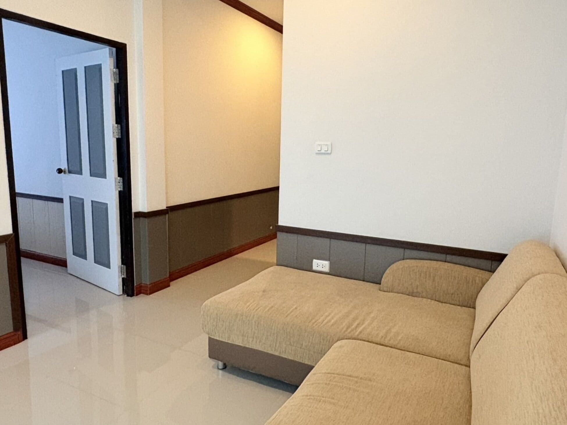 A room with a beige sofa, a door, and a wall with a light switch.
