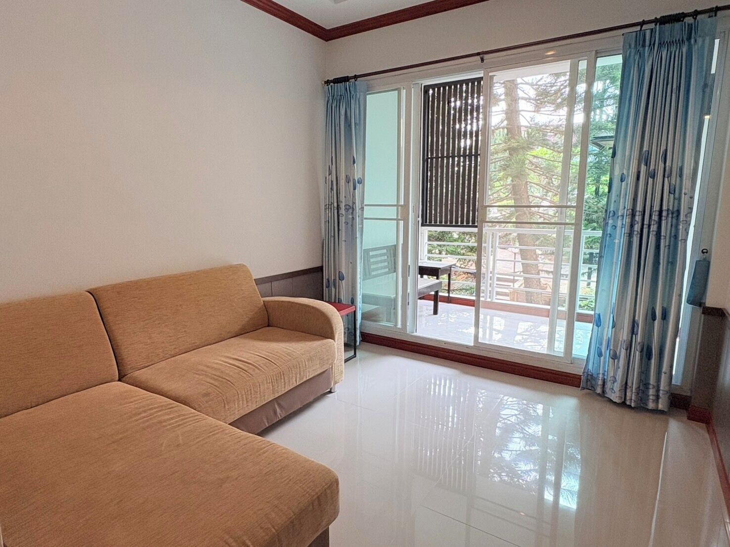 A room with a beige sofa, a small table, and a view through a sliding glass door to an outdoor area.