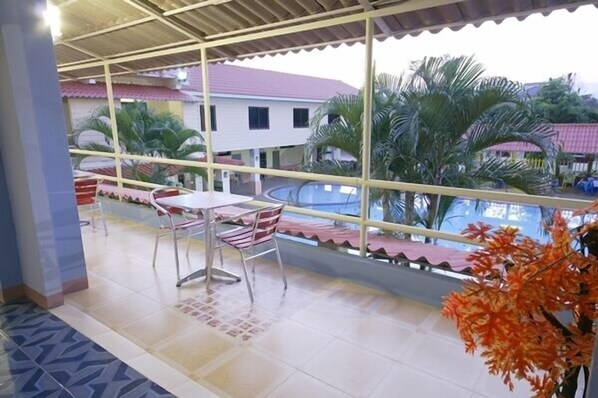 A balcony with a table and chairs, overlooking a swimming pool and palm trees.