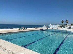 A swimming pool with clear blue water, a white bridge, and a view of the ocean.