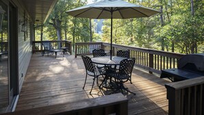 Un terrazzo in legno con un tavolo rotondo e sedie, un ombrellone e un barbecue.