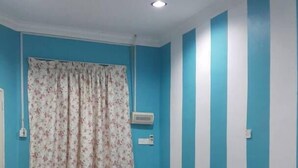 A room with a black leather sofa, a ceiling fan, and a window with floral curtains. - Noor Homestay (Kangar)
