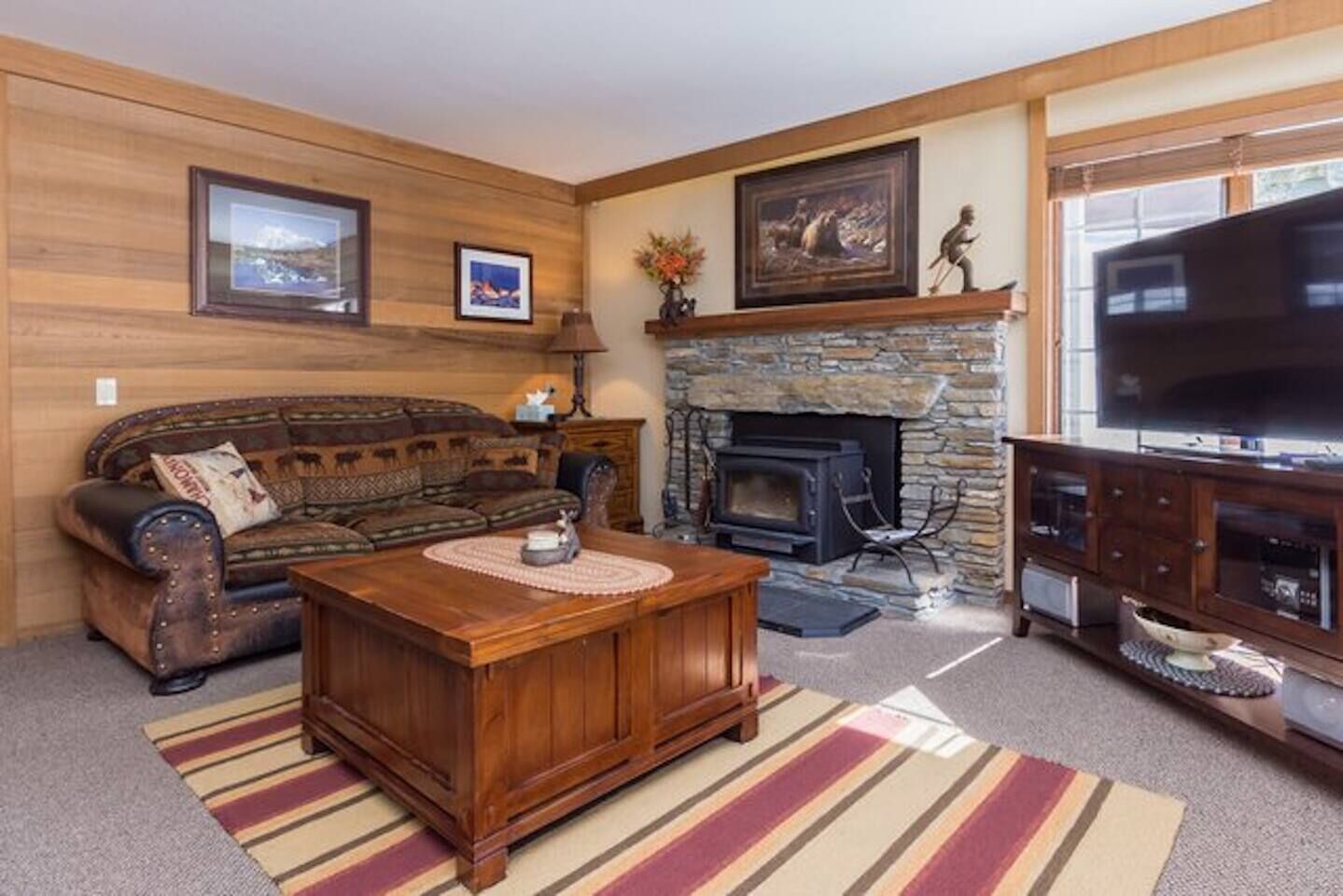 A cozy living room with a stone fireplace, a wooden sofa, a coffee table, and a television.