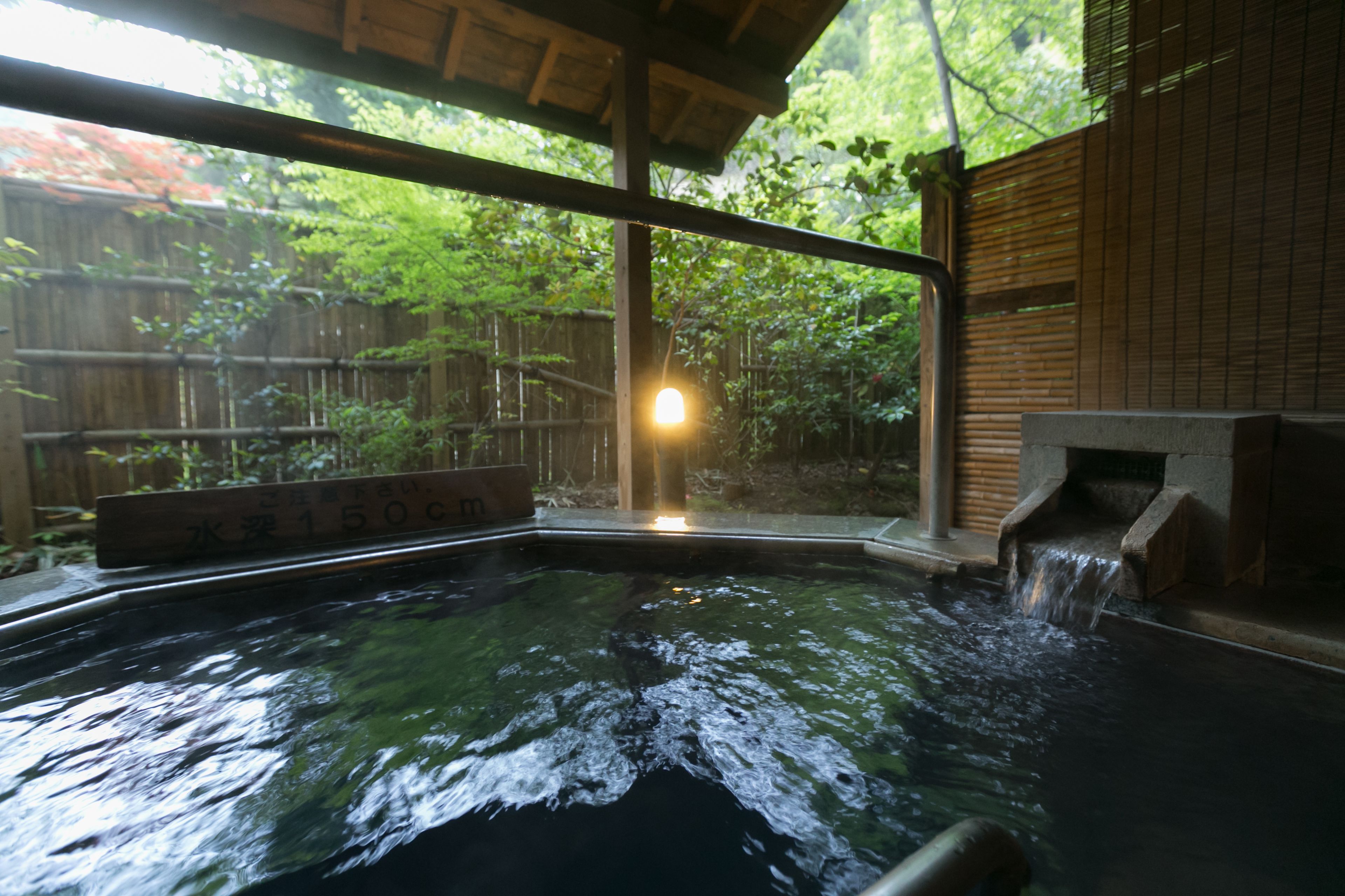 Un bain thermal en plein air, avec une structure en bois et une clôture en bambou en arrière-plan.