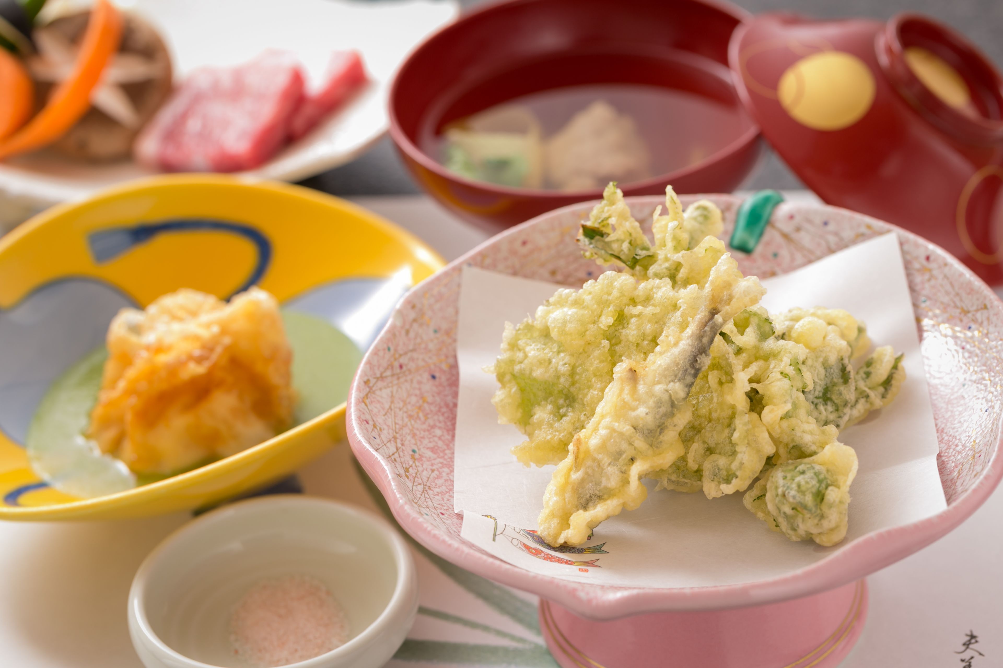 Una mesa con diversos platos, incluyendo tempura, sashimi y un tazón de arroz.