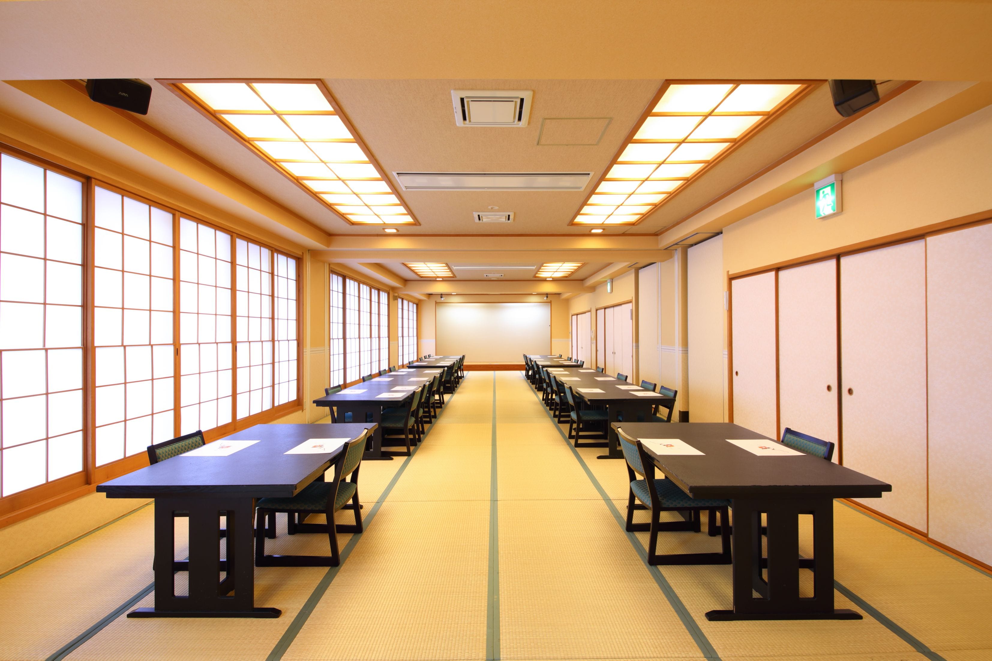 A conference room with long tables and chairs, large windows, and a tiled floor.