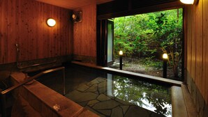A wooden interior with a stone hot tub and a view of a lush garden. - Kurokawa Onsen Yamabiko Ryokan (Minamioguni)