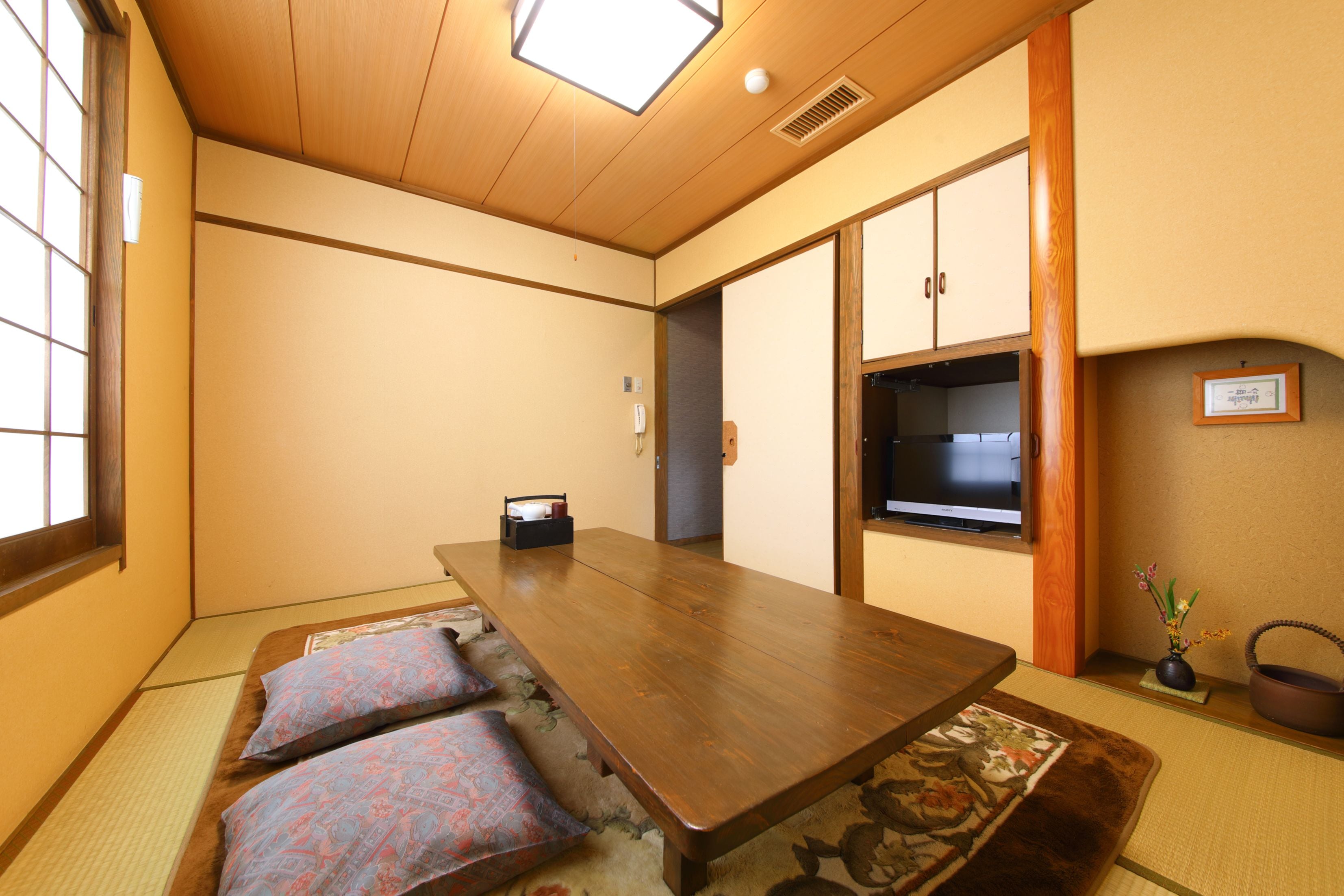 Una camera tradizionale in stile giapponese con pavimentazione in tatami, un tavolo di legno e una porta scorrevole che dà su un angolo cottura.