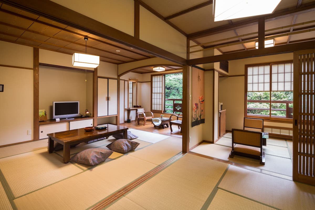 Una habitación japonesa tradicional con suelo de tatami, una mesa de madera baja, un televisor y una puerta corredera que da a un balcón.