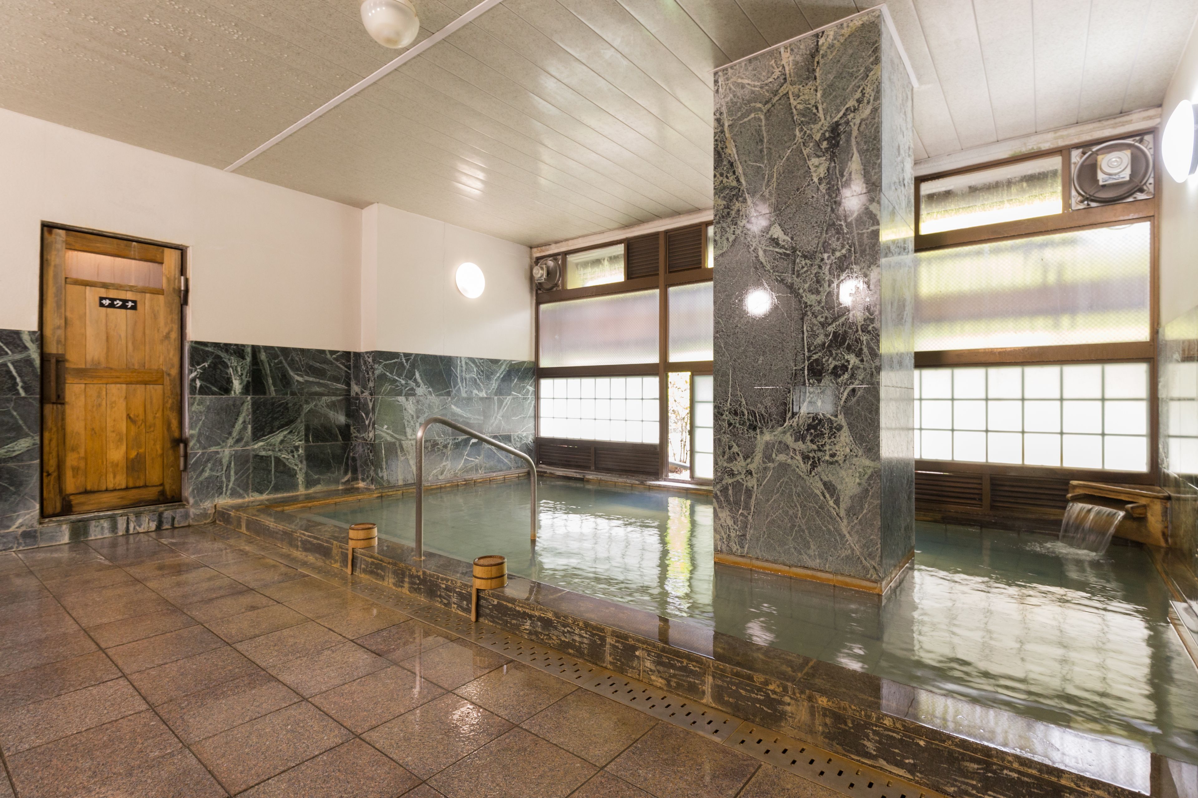 A traditional Japanese onsen with a wooden door, stone walls, and a tiled floor.