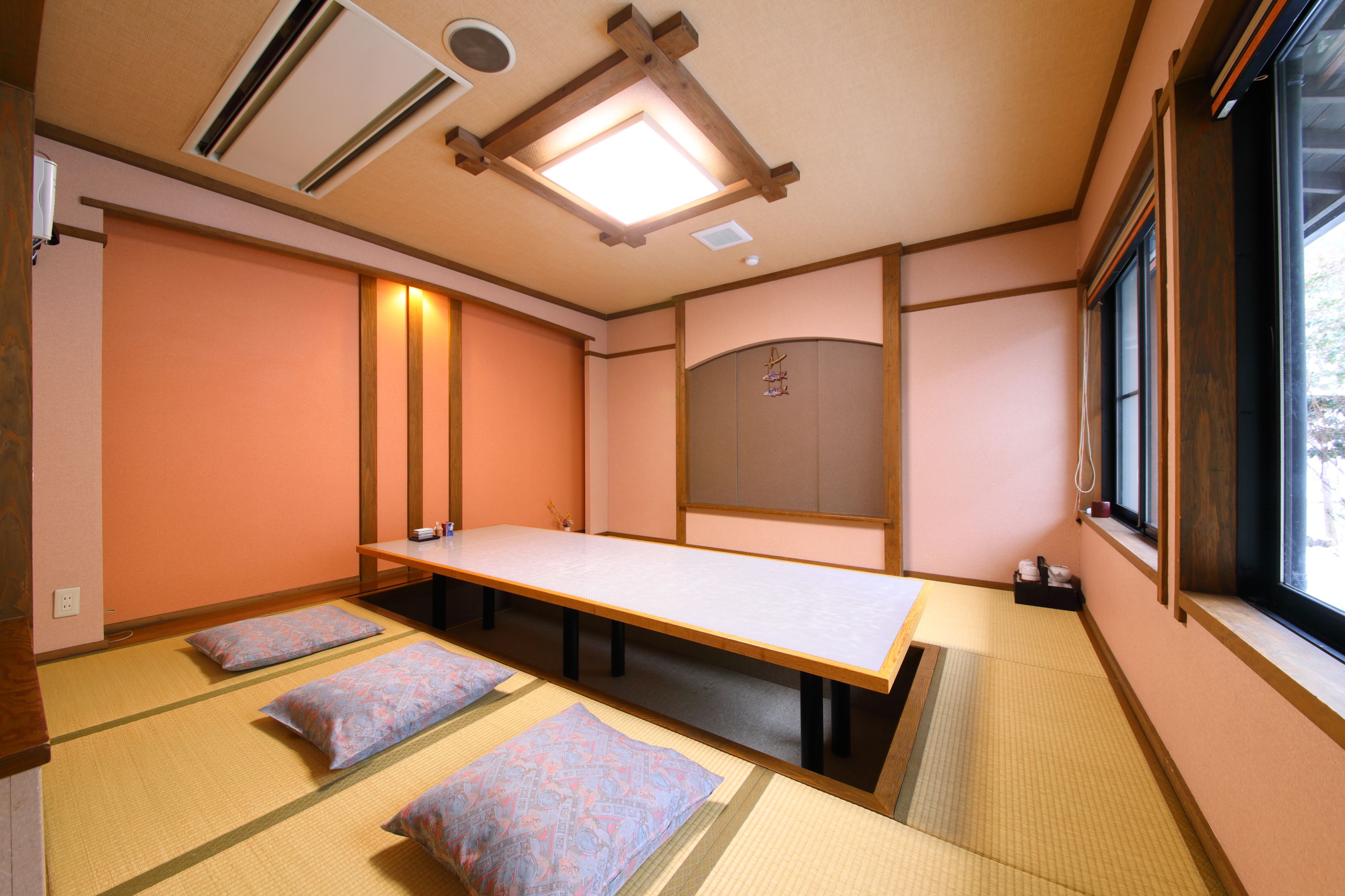 Une pièce avec un sol recouvert de tatamis, une petite table et des coussins, des poutres en bois au plafond et une fenêtre offrant une vue agréable.