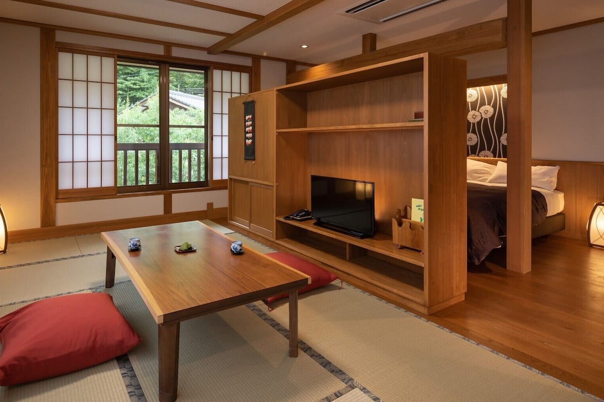 Una habitación japonesa tradicional con suelo de tatami, una mesa baja, un televisor y una cama con futón.