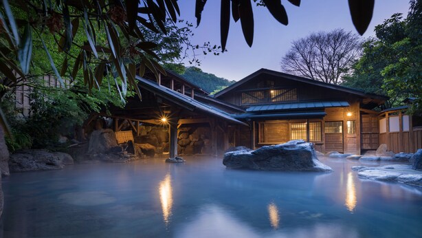 A traditional wooden building with a stone foundation, surrounded by a natural landscape with rocks and trees. - Kurokawa Onsen Yamabiko Ryokan (Minamioguni)