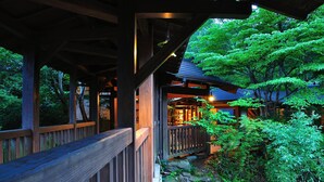 A wooden structure with a wooden deck and a stone pathway leading to a building with a blue roof. - Kurokawa Onsen Yamabiko Ryokan (Minamioguni)