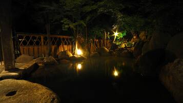 A tranquil outdoor setting with a wooden bridge, large rocks, and a pond reflecting lights.