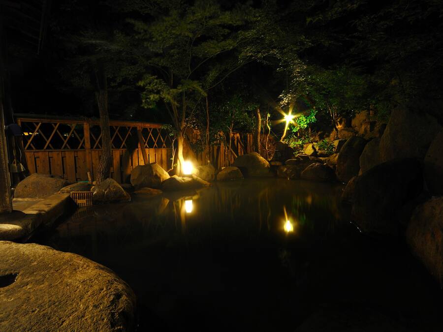 A tranquil outdoor setting with a wooden bridge, large rocks, and a pond reflecting lights.