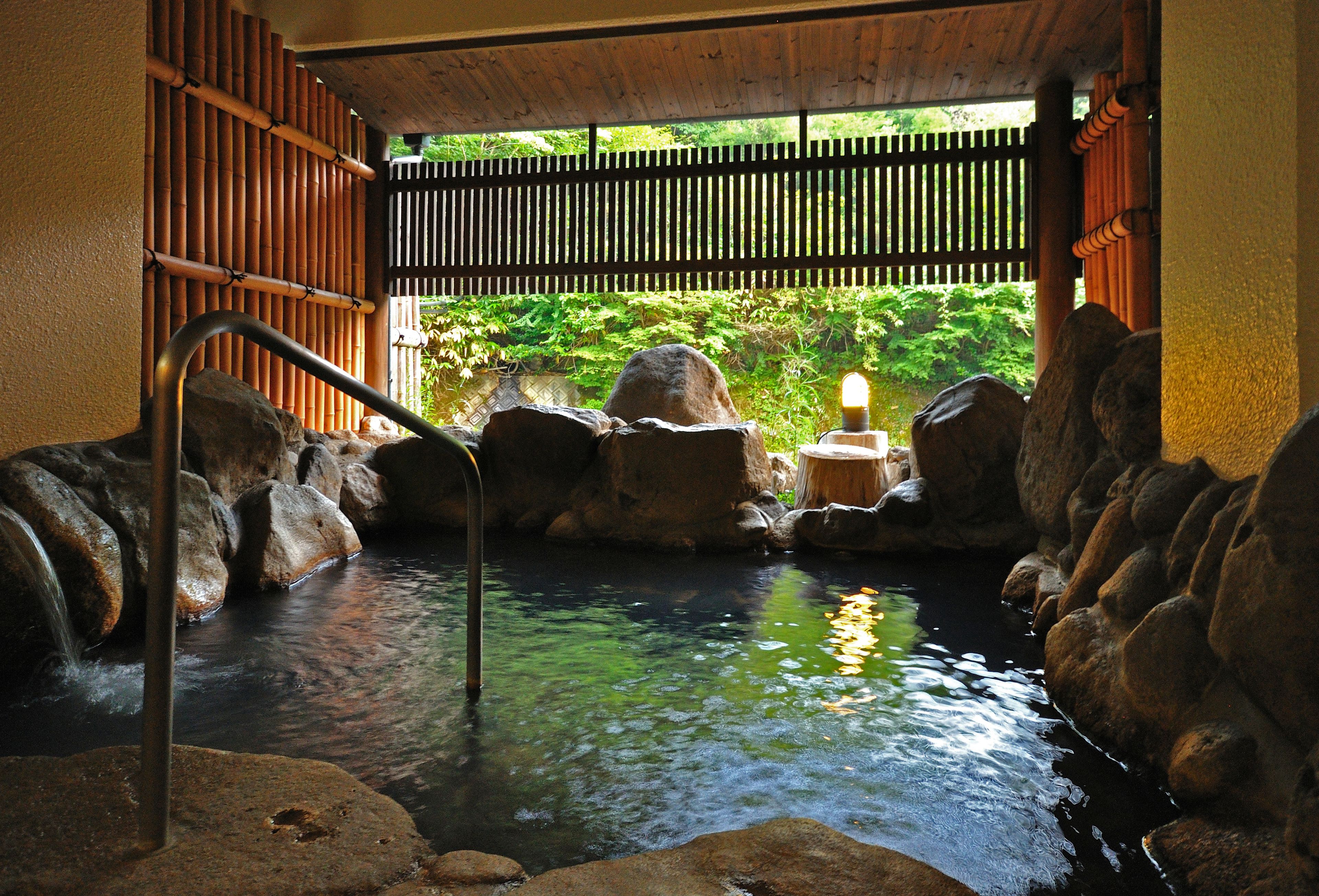 A tranquil indoor water feature with a wooden bridge, surrounded by rocks and bamboo walls.