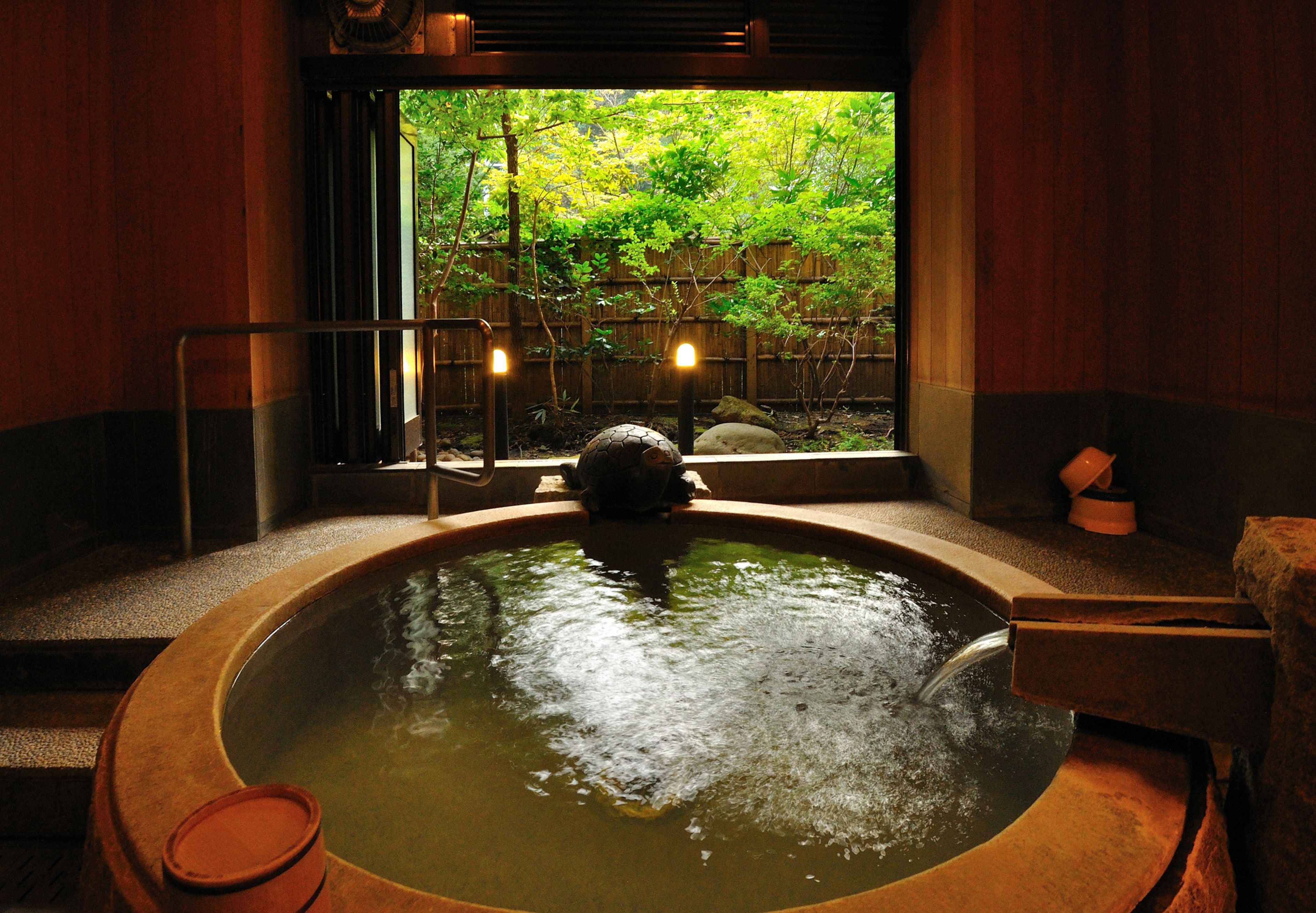 Un bain thermal à l’eau chaude avec un intérieur en bois, une vue sur la verdure environnante et une lanterne en pierre.