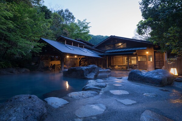 A traditional Japanese ryokan with a wooden exterior, a stone pathway leading to a hot spring, and a view of the surrounding forest.