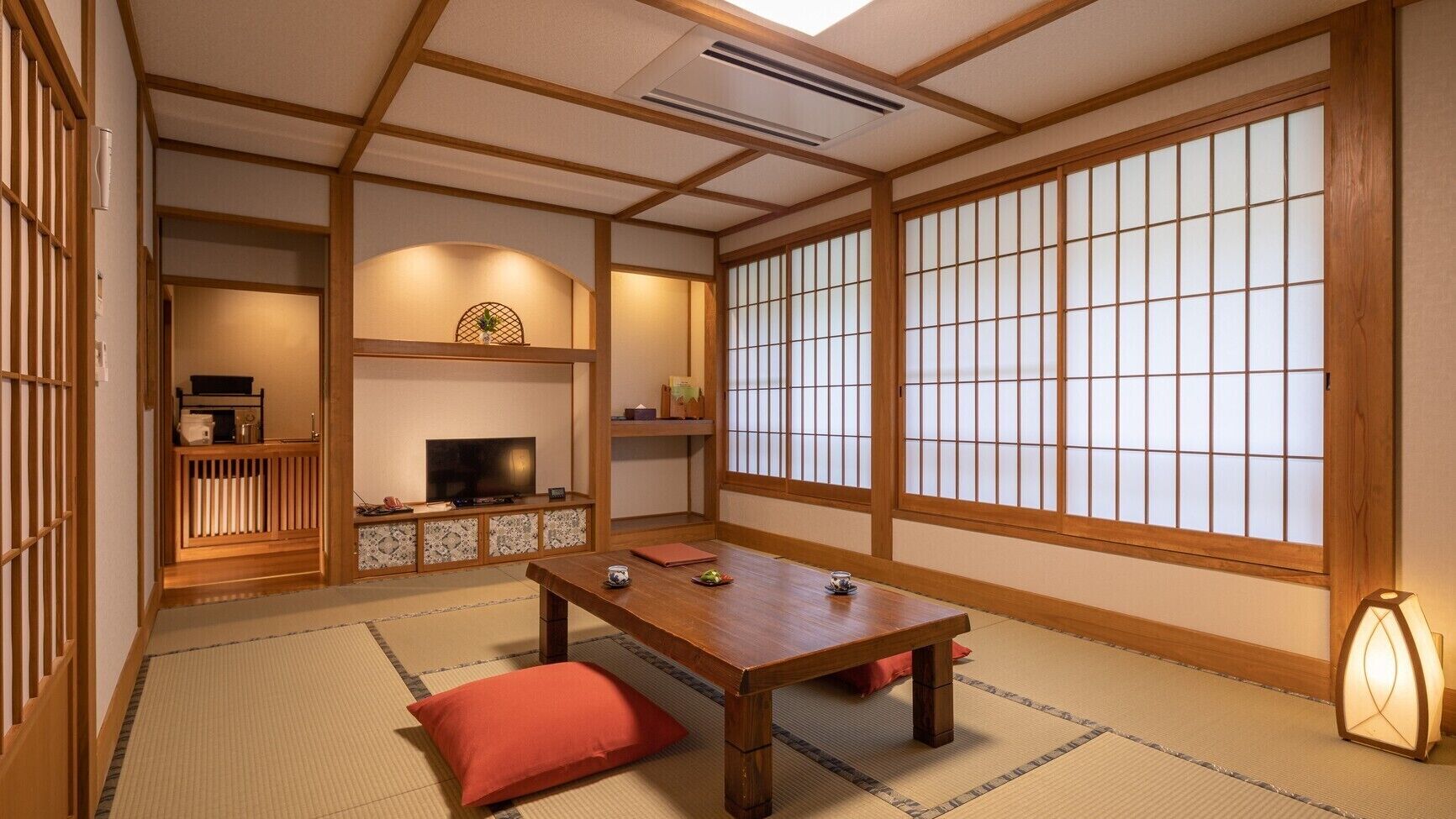 A traditional Japanese room with tatami flooring, a low table, a television, and sliding doors.