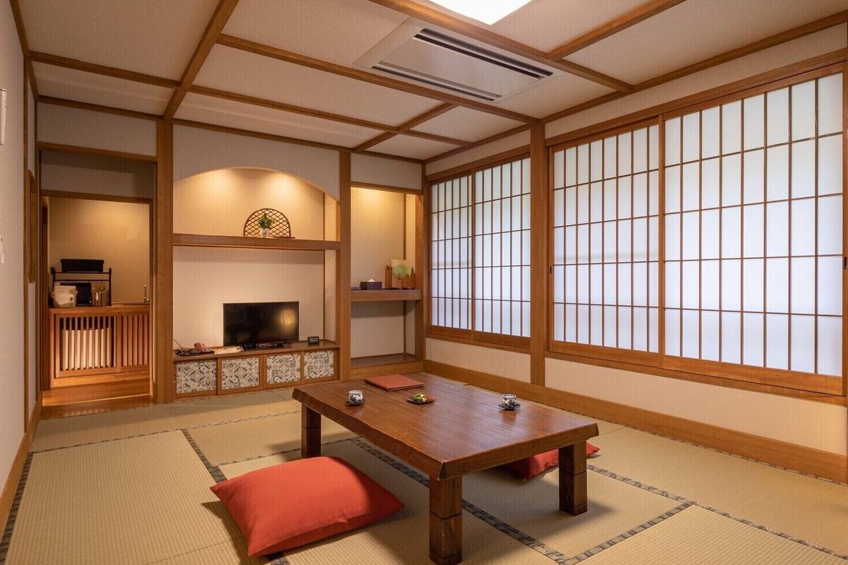 Una habitación japonesa tradicional con suelo de tatami, una mesa baja, un televisor y puertas correderas.