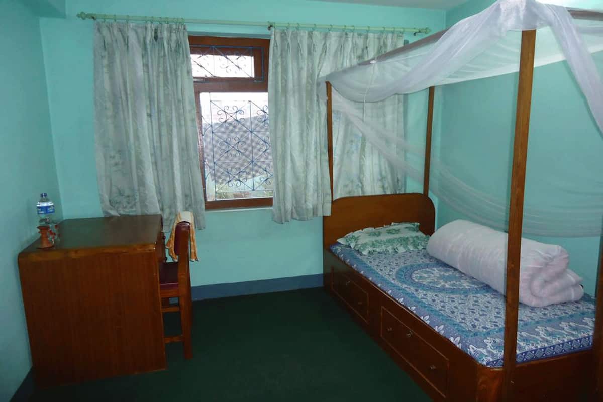 A bedroom with a four-poster bed, a wooden desk, and a window with curtains.