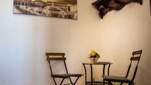 Un coin aménagé avec deux chaises pliantes, une petite table ornée d’un vase de fleurs et, au mur, un tableau représentant un bâtiment historique.