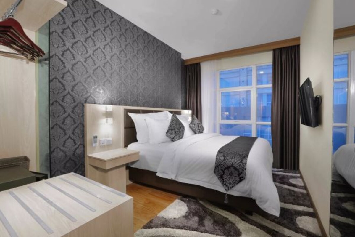 Una habitación de hotel moderna con una cama grande, una mesita de noche y un ventanal con cortinas, y una pared con diseño.