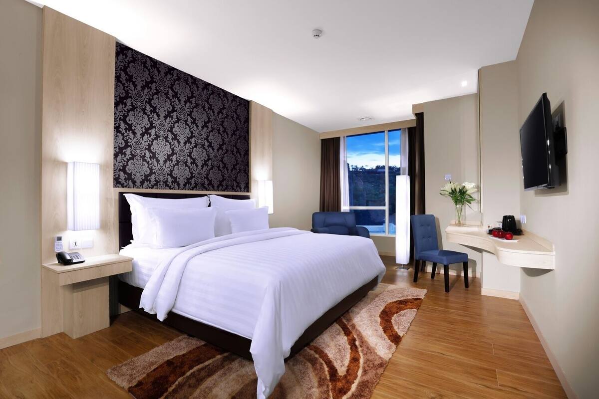 A hotel room with a large bed, bedside tables, a desk with a chair, a TV, and a window with a view.