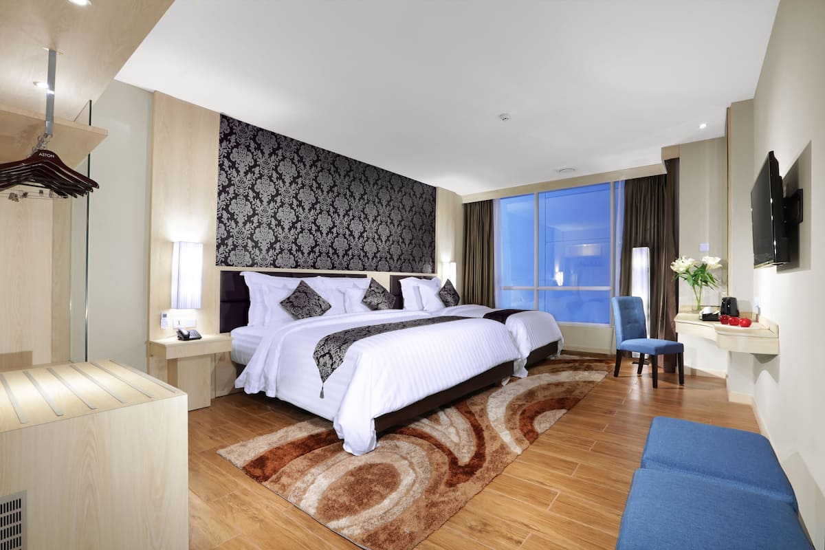 A modern hotel room with a large bed, a desk, a chair, and a TV.